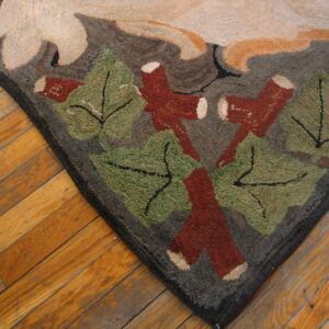 Textured rug corner with a botanical pattern in green, rust, beige, and gray on diagonal wood floorboards.