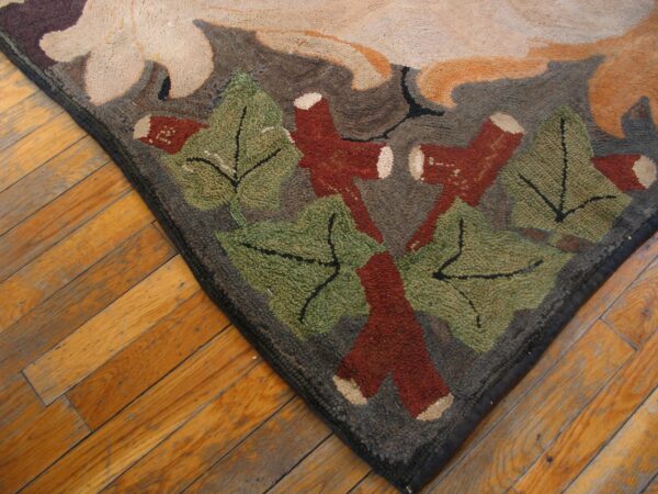 Textured rug corner with a botanical pattern in green, rust, beige, and gray on diagonal wood floorboards.