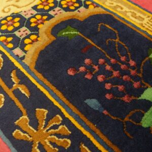 Plush rug detail showing navy blue field, gold scrolling borders, green foliage, and maroon floral accents on pink flooring.