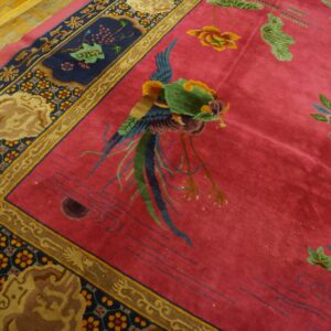 Vibrant magenta rug with a central green bird, floral motifs, and an intricate navy blue border on wood floors.