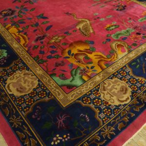 Plush magenta rug with crane and floral motifs, bordered in navy, gold, and tan on wood planks.