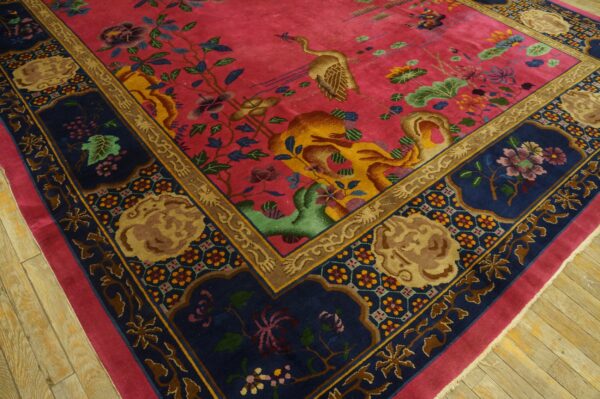 Plush magenta rug with crane and floral motifs, bordered in navy, gold, and tan on wood planks.