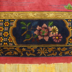Ornate high-pile rug detail showing a navy medallion with pink flowers and a large red border on wood flooring.