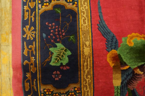Detail of a colorful rug showing a navy border panel with berries and a magenta field with a partial green bird.