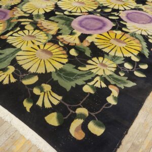 Close view of a black rug featuring large yellow and purple floral patterns on light plank wood flooring.