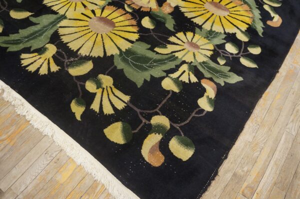 Close up of a black rug detailed with large yellow flowers and green leaves on wood flooring.