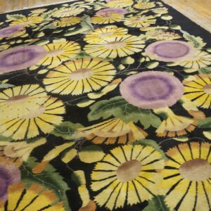Vibrant yellow and purple floral pattern on a black rug laid out on wooden floorboards.