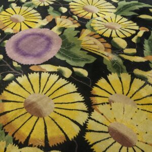 A high-pile black rug with large yellow, purple, and green florals resting on light wood flooring.