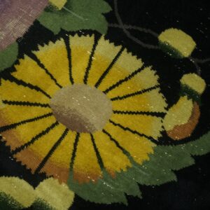 Close-up of a dark rug showing a prominent yellow sunflower surrounded by green leaves and purple detail.