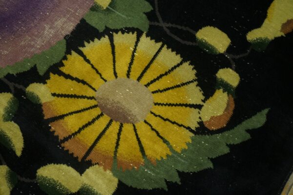 Close-up of a dark rug showing a prominent yellow sunflower surrounded by green leaves and purple detail.