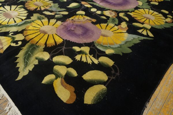 Black rug with high pile, patterned with bold yellow, green, and purple flowers on wood flooring.