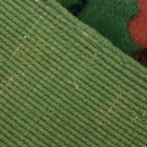 View of the rug reverse showing ribbed light green weaving and fringe next to the deep pile green, red, and brown pattern.