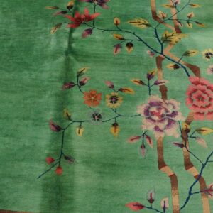 Teal green rug with a stylized pink, purple, and yellow floral pattern resting on distressed wood floor.