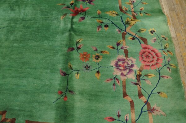 Teal green rug with a stylized pink, purple, and yellow floral pattern resting on distressed wood floor.