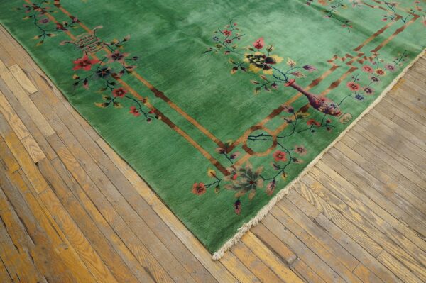 A bright green rug featuring colorful floral motifs and tan borders rests on distressed wood flooring.