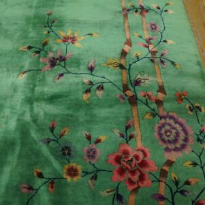 Medium-pile green rug displays colorful floral motifs and brown bamboo on rustic wood planks.