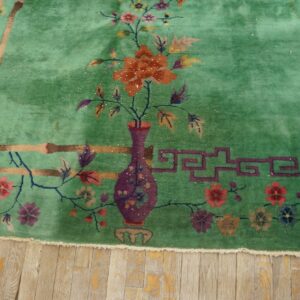 Mint green plush rug with an orange flower vase and bamboo patterns on light distressed wood.