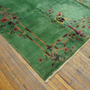 Corner of a bright green rug with floral and brown lattice patterns, placed on worn wooden flooring.