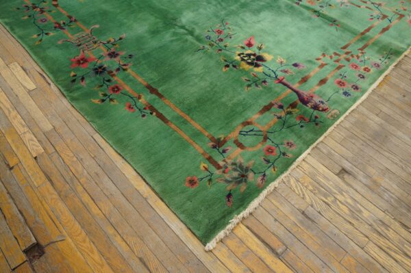 Corner of a bright green rug with floral and brown lattice patterns, placed on worn wooden flooring.