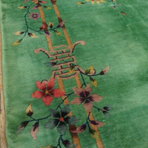 Bright green plush rug with a red, pink, and yellow floral pattern borders worn wooden planks.