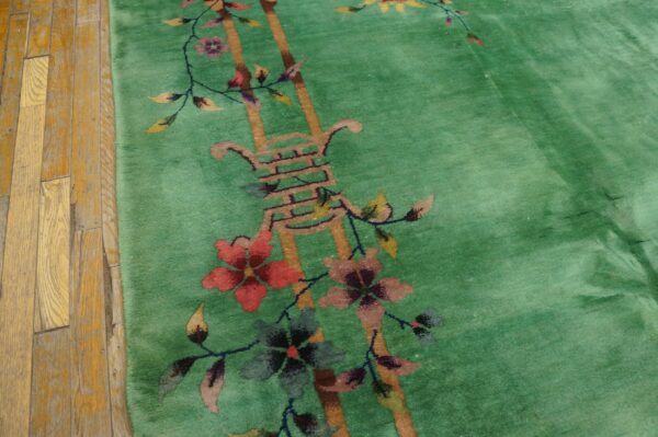 Bright green plush rug with a red, pink, and yellow floral pattern borders worn wooden planks.