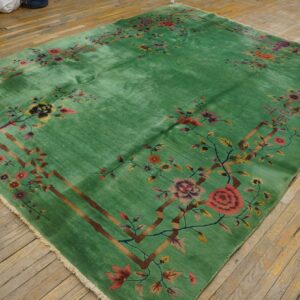 High-sheen green rug featuring a detailed border of multicolored flowers and brown branches on distressed wood planks.