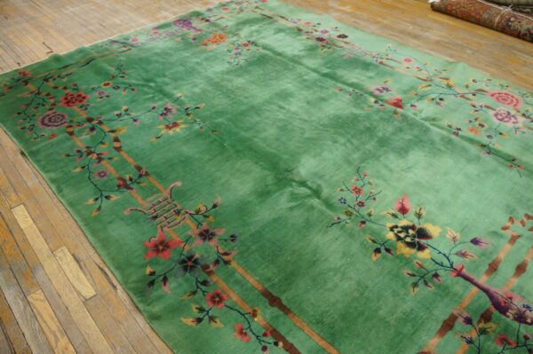 Jade green rug with high pile and multicolored floral, vine, and bamboo patterns on wood floor.