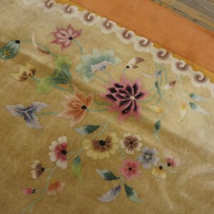 Shimmering golden rug featuring a multicolored floral design, scrolled border, and wide orange edge on wood floor.