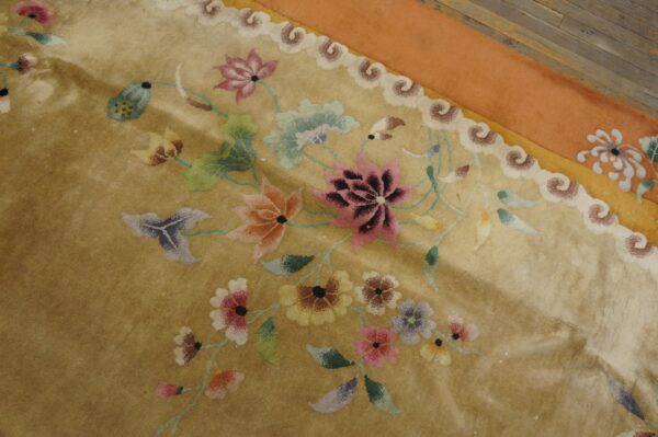 Shimmering golden rug featuring a multicolored floral design, scrolled border, and wide orange edge on wood floor.