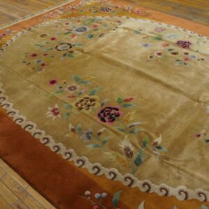 Golden floral rug with scalloped border and rust field sits on distressed hardwood floor.