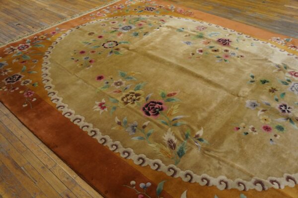 Golden floral rug with scalloped border and rust field sits on distressed hardwood floor.