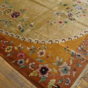 Gold high-pile rug with colorful floral motifs and an orange border rests on worn wood flooring.