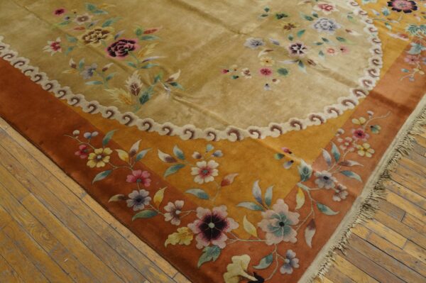 Gold high-pile rug with colorful floral motifs and an orange border rests on worn wood flooring.