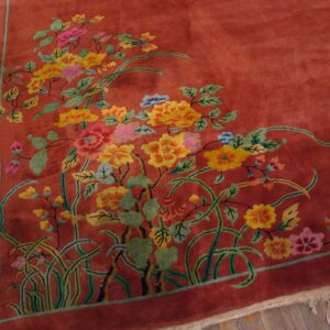 A rust-colored rug corner featuring a dense floral pattern in yellow, pink, and green on wooden flooring.