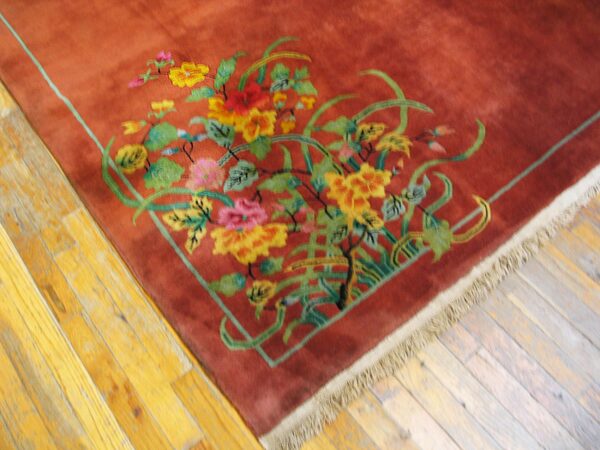 Close-up of a high-pile rust rug with bright floral and vine designs on worn yellow wood planks.