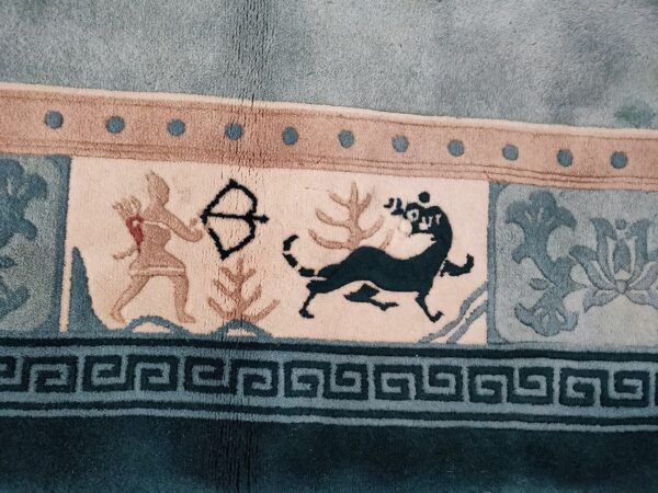 Teal and tan rug border features a greek key design, archer figure, and running stylized animal motifs.