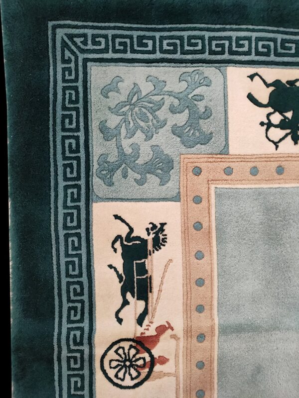 Corner detail of a plush rug featuring teal borders, greek key design, and figurative historical motifs.