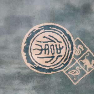 Muted teal rug with carved beige medallions, dark blue motifs, and a vertical polka dot border.