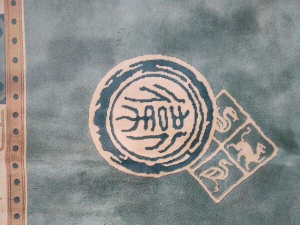 Muted teal rug with carved beige medallions, dark blue motifs, and a vertical polka dot border.