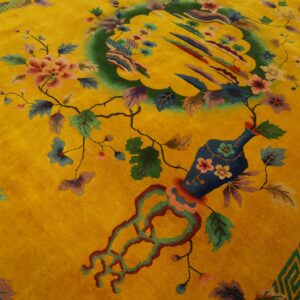 A yellow rug displays a complex pattern of flowering vines, a vase, and a central green scenic medallion.