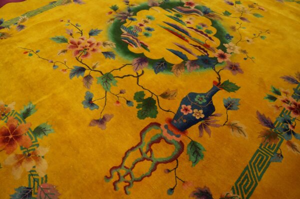 A yellow rug displays a complex pattern of flowering vines, a vase, and a central green scenic medallion.