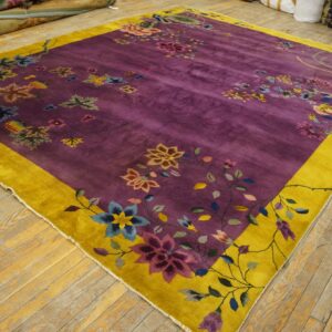 A purple and gold floral rug with a medium pile lies on distressed wood floors.