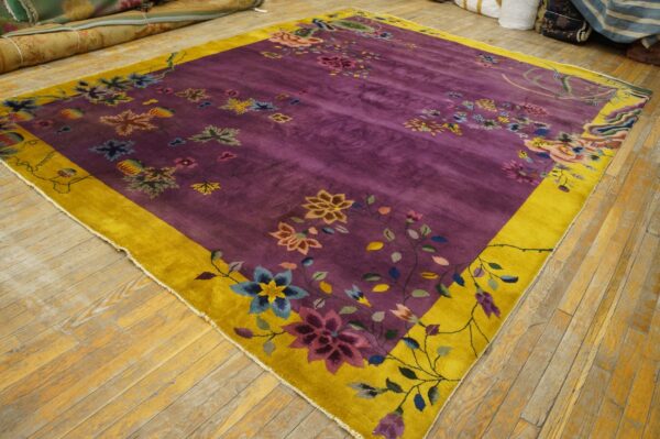 A purple and gold floral rug with a medium pile lies on distressed wood floors.