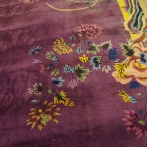 A deep purple rug with a multicolored floral pattern and a bright yellow border rests on wood planks.