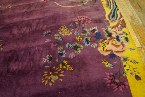 A deep purple rug with a multicolored floral pattern and a bright yellow border rests on wood planks.