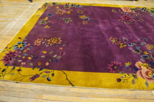 A large purple floral rug with a bright gold border rests on worn wooden plank flooring.