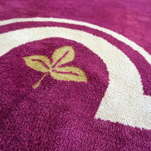 Shaggy magenta rug featuring a gold leaf motif and thick, curving borders in creamy white.