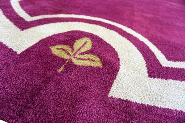 Shaggy magenta rug featuring a gold leaf motif and thick, curving borders in creamy white.