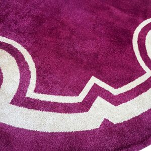 Close-up of a magenta high-pile rug detail featuring thick cream geometric borders and small golden leaf elements.