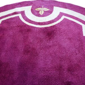 Close-up of a deep purple shag rug with a white, stylized geometric border and small leaf.